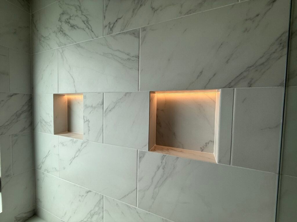 Large-format marble-look tile shower wall with LED-lit niches